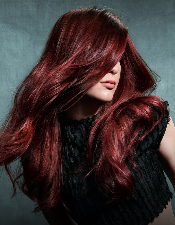 A woman with long, vibrant dark red hair. - Salon Aria + Spa in Davenport, IA