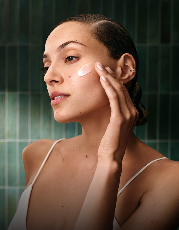 A woman applying a dab of cream to her cheekbone. - Salon Aria + Spa in Davenport, IA